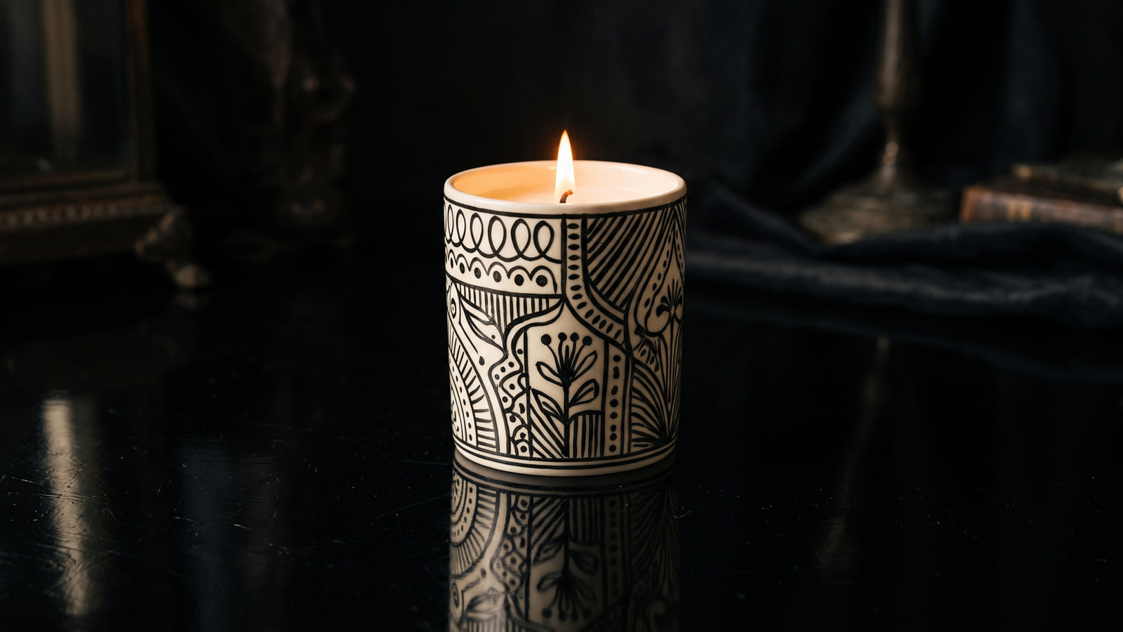 Fornasetti style hand-decorated porcelain candle on a dark lacquered surface